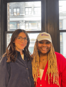 Two Remy team members smiling by an office window, one wearing a white Remy cap